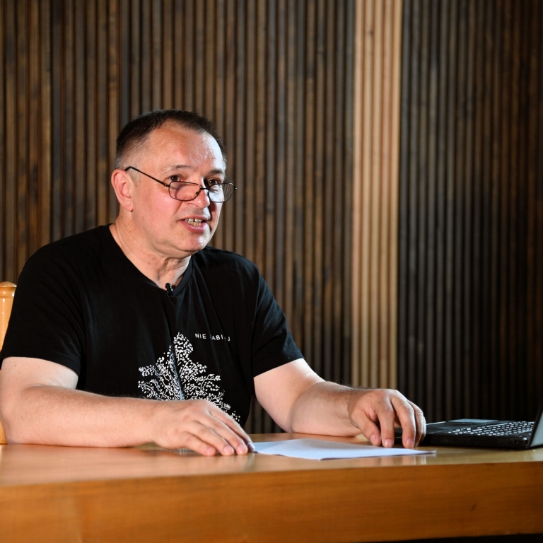 Wojciech Birek siedzi w czarnej koszulce w sali WDK w Rzeszowie w czasie wykładu który prowadzi